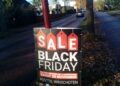 When Is Black Friday 2026? Thanksgiving and Cyber Monday Dates Shoppers carrying bags past a store window with sale signs during the holiday shopping season