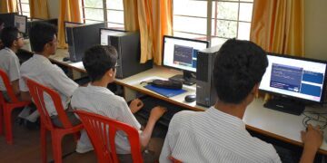 Student holding a school marksheet and certificate papers at a desk